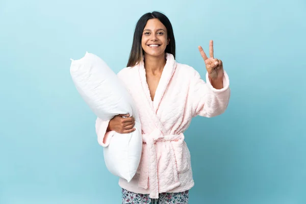 Young woman in pajamas over isolated background in pajamas and smiling while showing victory sign