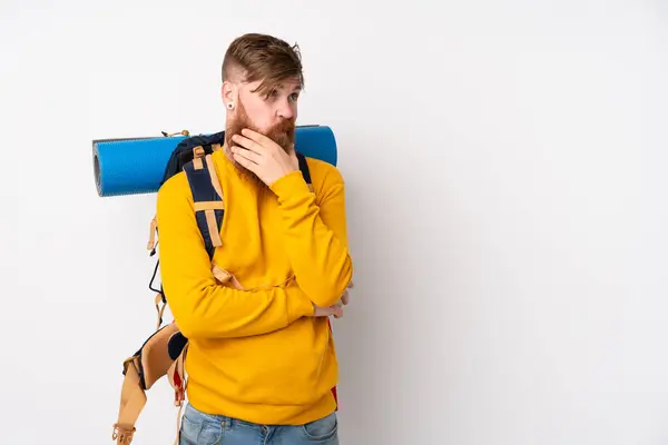 Young mountaineer man with a big backpack over isolated white background thinking an idea