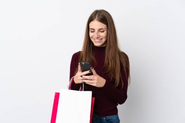 Elinde alışveriş poşetleri olan ve cep telefonuyla bir arkadaşına mesaj yazan izole edilmiş beyaz bir arka plan.