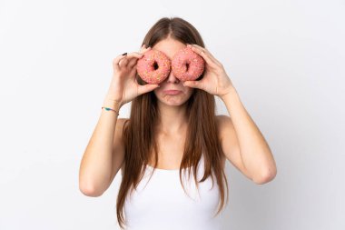 Soyutlanmış beyaz arka planda genç bir kadın üzgün bir ifadeyle gözlerinde donut tutuyor.