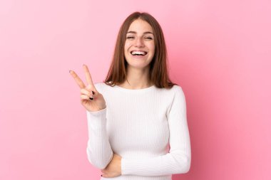 Soyutlanmış pembe arka planda genç bir kadın gülümsüyor ve zafer işareti gösteriyor