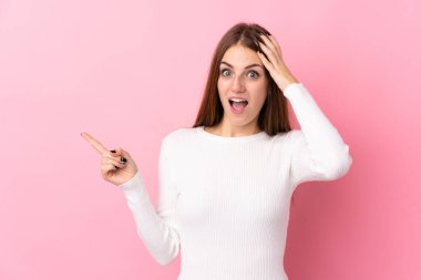 Soyutlanmış pembe arka planı olan genç bir kadın şaşırmış ve işaret ediyor.