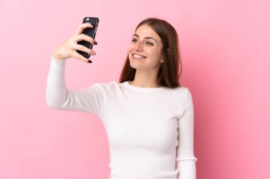 Soyutlanmış pembe arka planı olan genç bir kadın selfie çekiyor.