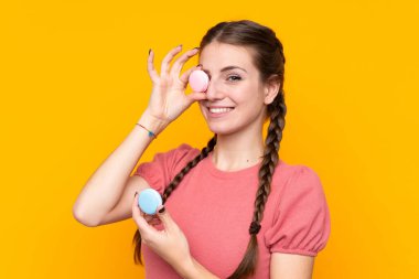 Renkli Fransız badem kurabiyeleriyle izole edilmiş sarı arka planı olan genç bir kadın.