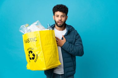 Genç Faslı bir adam, izole edilmiş arka planda geri dönüşüm yapmak için elinde plastik şişelerle dolu bir çanta tutuyor.