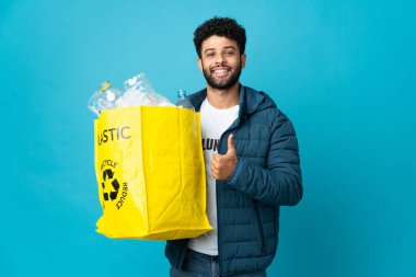Genç Faslı bir adam, izole edilmiş arkaplanı geri dönüştürmek için plastik şişelerle dolu bir çanta tutuyor.