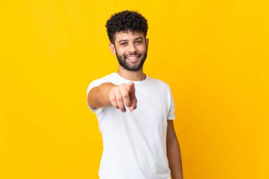 Sarı arka planda izole edilmiş genç Faslı adam mutlu bir ifadeyle cepheyi işaret ediyor