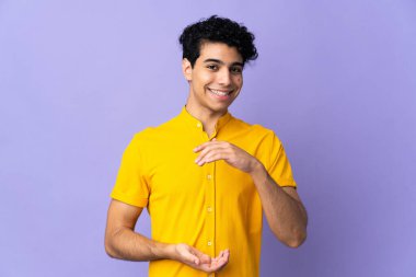 Genç Venezuelalı bir adam, mor arka planda izole edilmiş bir şekilde, bir ilan vermek için, fotokopi uzayı avucunun içinde tutuyor.