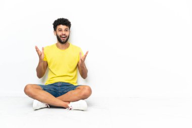 Genç Faslı yakışıklı bir adam yerde izole edilmiş bir şekilde oturuyor ve yüzünde sürpriz bir ifade var.