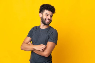 Sarı arka planda izole edilmiş, kolları bağlı ve mutlu genç Faslı bir adam.
