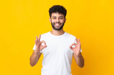 Sarı arka planda izole edilmiş genç Faslı iki elle tamam işareti gösteriyor.