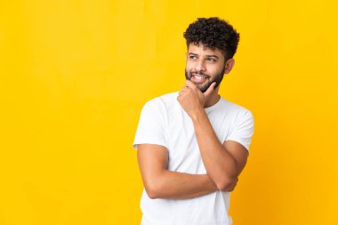 Genç Faslı adam sarı arka planda izole edilmiş gülümserken yukarı bakıyor.