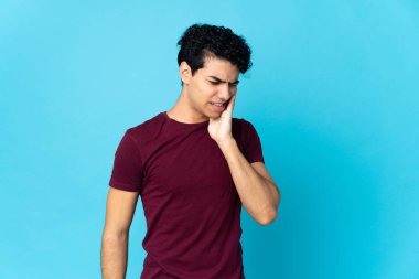 Genç Venezuelalı adam mavi arka planda diş ağrısı ile izole edilmiş.