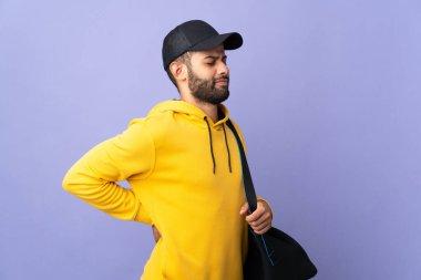 Spor çantalı genç Faslı adam, gayret gösterdiği için sırt ağrısından muzdarip mor arka planda izole edilmiş.