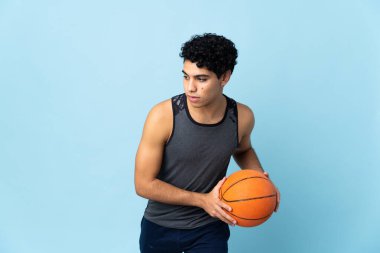 Genç Venezuelalı adam mavi arka planda izole edilmiş basketbol oynuyor.