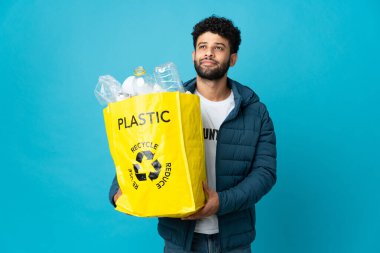 Genç Faslı bir adam izole edilmiş arka planı geri dönüştürmek için plastik şişelerle dolu bir çanta tutuyor.