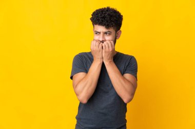 Faslı genç bir adam sarı arka planda izole edilmiş gergin ve korkmuş bir şekilde elleriyle suni teneffüs yapıyor.