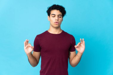 Genç Venezuelalı adam Zen pozunda mavi arka planda izole edilmiş.