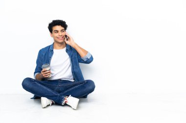 Venezuelalı bir adam kahve alıp götürmek için yerde oturuyor. Bir de cep telefonu.