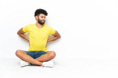 Genç Faslı yakışıklı bir adam, izole bir arka planda, yerde oturuyor. Çabaladığı için sırt ağrısı çekiyor.