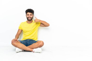 Genç Faslı yakışıklı bir adam izole bir zeminde oturuyor ve telefon jesti yapıyor. Bana geri dönüş işareti ver.