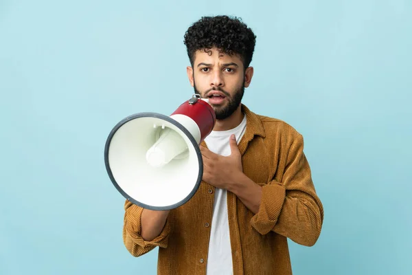 Young Moroccan man isolated on blue background shouting through a megaphone with surprised expression