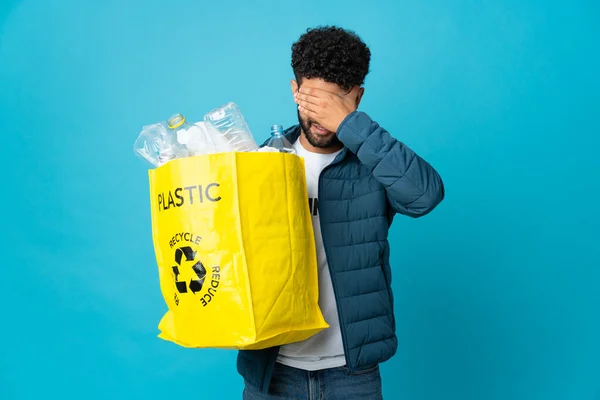 Young Moroccan man holding a bag full of plastic bottles to recycle over isolated background covering eyes by hands. Do not want to see something