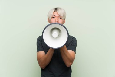 Yeşil arka planda genç Asyalı bir adam megafondan bağırıyor.