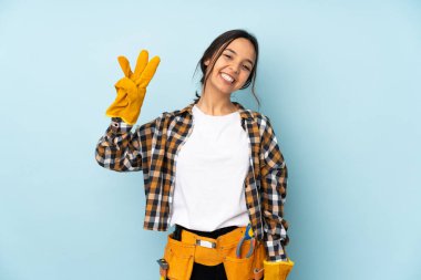 Mavi arka planda izole edilmiş genç elektrikçi kadın mutlu ve parmaklarıyla üçe kadar sayıyor.