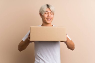 Asyalı genç bir adam izole edilmiş bir arkaplanı başka bir yere taşımak için bir kutu tutuyor.