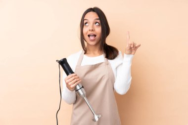 Genç esmer kız, el blendırını izole arka planda kullanıyor. Çözümü bulmak için parmağını kaldırıyor.