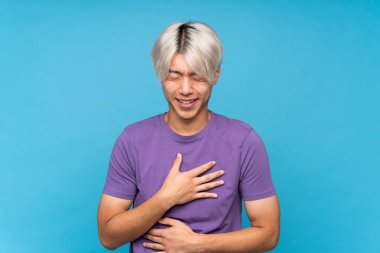 Soyutlanmış mavi arka planda genç Asyalı adam çok fazla gülümsüyor.