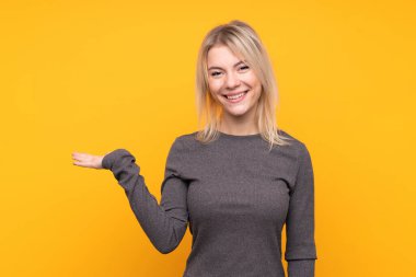 Sarışın, izole edilmiş sarı arka plan üzerinde genç bir kadın. Bir ilan vermek için avucunun içinde hayali bir alan tutuyor.