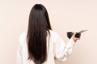 Arka planda bej rengi arka planda izole edilmiş genç Hintli bir kadın elinde çubuklarla bir kase erişte tutarken