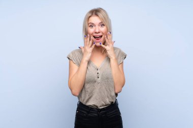 Soyutlanmış mavi arka planda, yüzünde sürpriz ifade olan genç sarışın kadın.