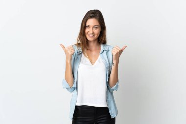 Beyaz arka planda izole edilmiş genç İrlandalı bir kadın. Baş parmakları havada ve gülümsüyor.