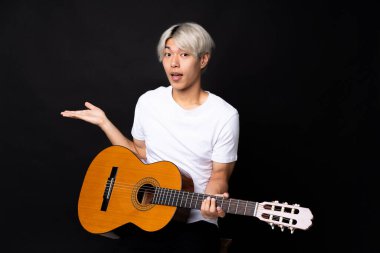 Siyah arka planda gitar çalan Asyalı genç bir adam.