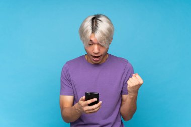 Asyalı genç adam izole edilmiş mavi arka plan şaşırdı ve bir mesaj gönderiyor.