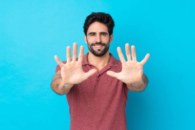 Sakallı, genç ve yakışıklı bir adam mavi arka planda parmaklarıyla ona kadar sayıyor.