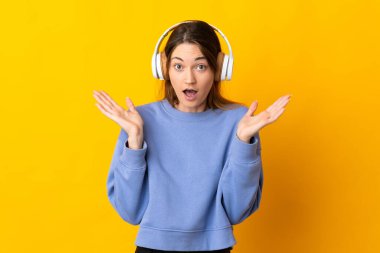Sarı arka planda izole edilmiş genç İrlandalı kadın şaşırdı ve müzik dinliyor