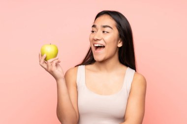 Genç Hintli bir kadın pembe arka planda yalnız ve mutlu bir elmayla