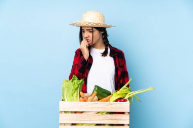 Genç çiftçi kadın taze sebzeleri ahşap bir sepette tutuyor. Şüpheleri var.