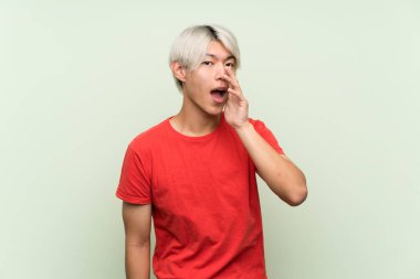 Tecrit edilmiş yeşil arka planda genç Asyalı adam ağzı açık bağırıyor.