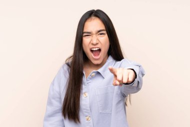 Bej arka planda izole edilmiş genç Hintli kadın hayal kırıklığına uğramış ve ön tarafı işaret ediyor.