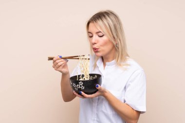 Genç Rus kadın izole arka planda elinde yemek çubuğuyla bir kase erişte tutuyor ve sıcak oldukları için üflüyor.