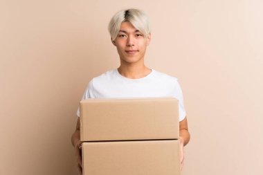 Asyalı genç bir adam izole edilmiş bir arkaplanı başka bir yere taşımak için bir kutu tutuyor.