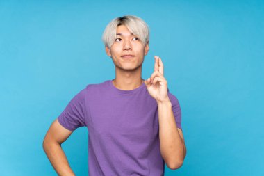 Asyalı genç adam izole edilmiş mavi arka planda şans diliyor ve en iyisini diliyor.