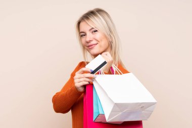 Soyutlanmış bir geçmişi olan genç sarışın bir kadın alışveriş torbaları ve bir kredi kartı tutuyor.