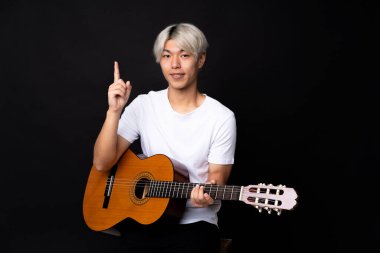 Siyah arka planda gitarı olan Asyalı genç adam harika bir fikre işaret ediyor.
