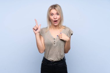 Soyutlanmış mavi arka planda, yüzünde sürpriz ifade olan genç sarışın kadın.